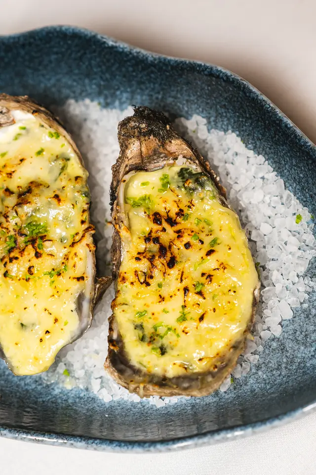Ostiones Rockefeller gratinados con queso dorado sobre sal de grano en plato azul