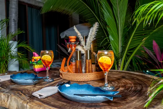 Mesa nocturna para dos con cocteles spritz y platos azules en el patio selvático de MERO 18