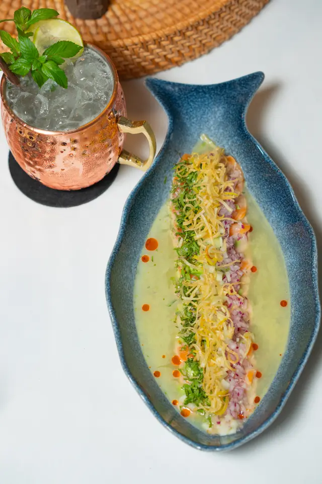 Tiradito de salmón en leche de tigre con cilantro y poro crujiente en plato azul