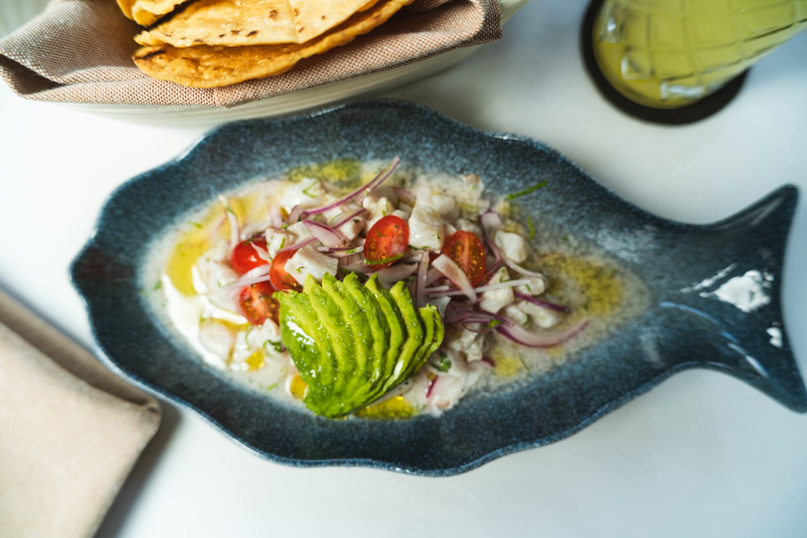 Ceviche de pesca del día con abanico de aguacate en plato azul con forma de pez, servido con tostadas en MERO 18, Centro de Cancún