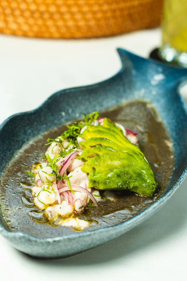 Aguachile negro con pescado fresco, abanico de aguacate y cebolla morada en plato con forma de pez