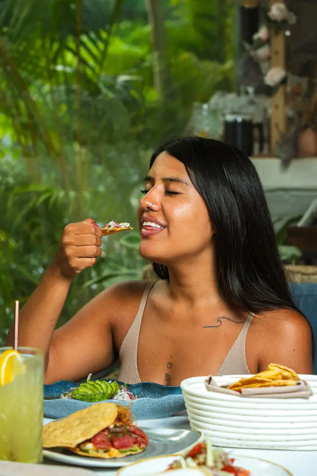 Comensal disfrutando una tostada de ceviche con los ojos cerrados entre el follaje del patio