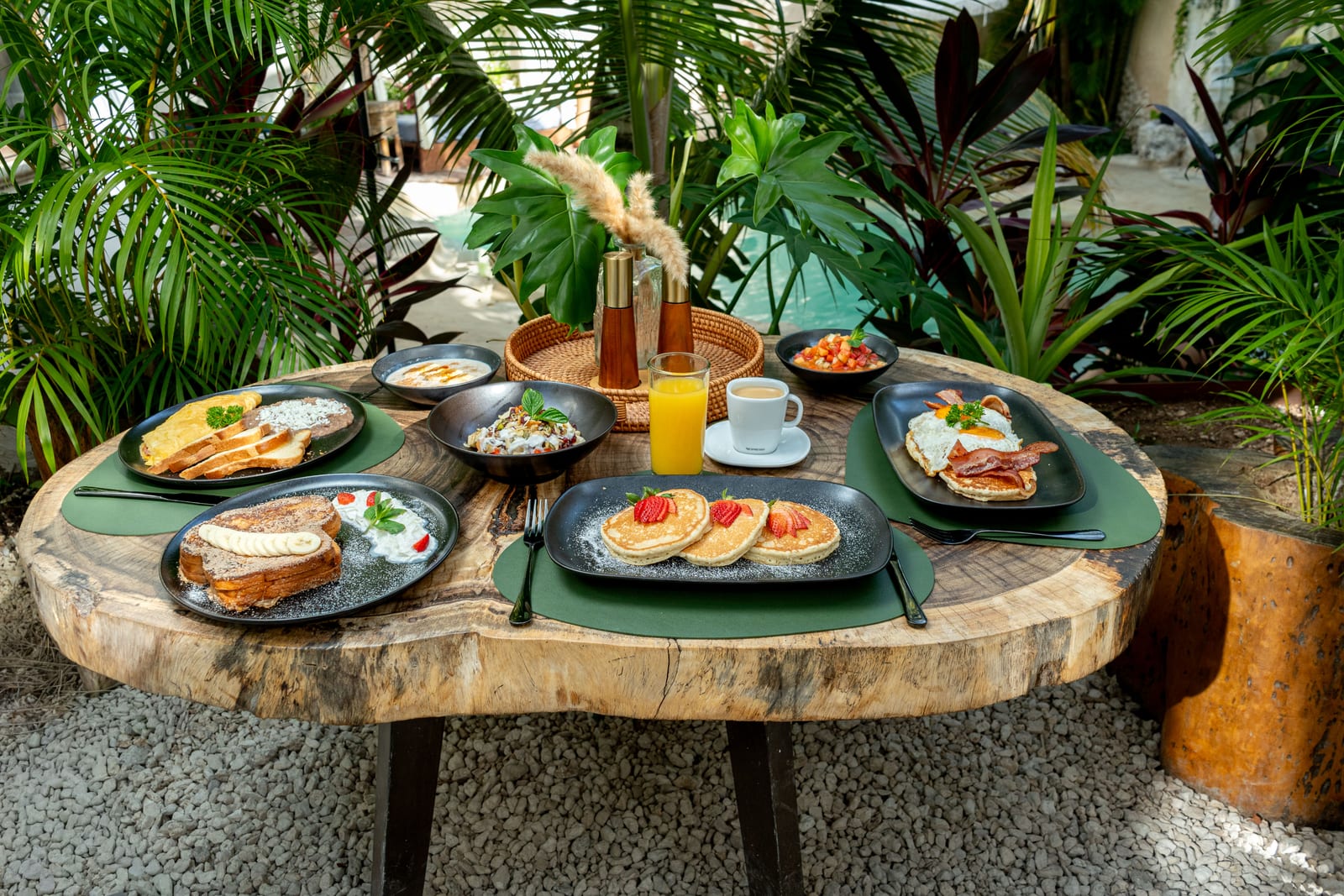Mesa de desayuno de MERO 18 en el jardín selvático junto a la alberca cenote, con hotcakes, pan francés y jugos