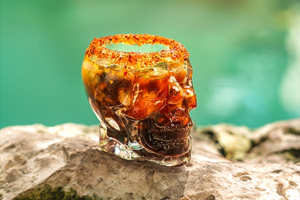 Shot de mariscos servido en cráneo de cristal con borde de chile junto a la alberca